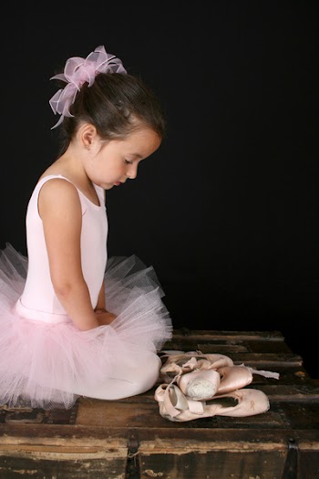 Beautiful brunette girl wearing a pink tutu sitting by pointe shoes