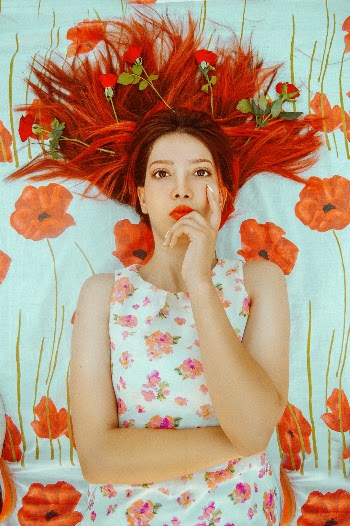 Beautiful fine art portrait of a ginger model laying on the ground spreading her long beautiful hair filled with red roses.