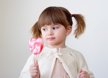 Beautiful little girl holding a big heart shaped lollipop