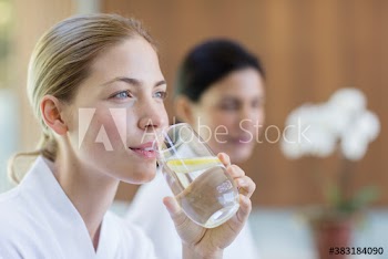 Beautiful young woman drinking lemon water in spa