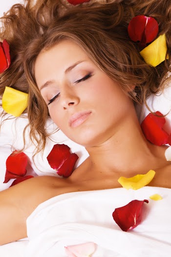 Beautiful young woman lying in rose petals, face closeup