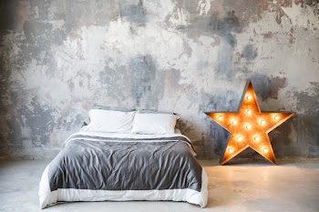 Bedroom in loft style and gray colors. Metal star with lamps and a bed near gray plaster wall