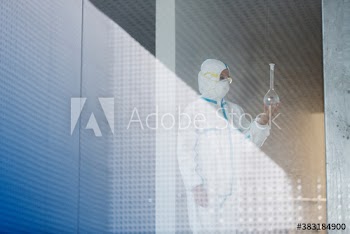 Biochemist in clean suit examining beaker with liquid