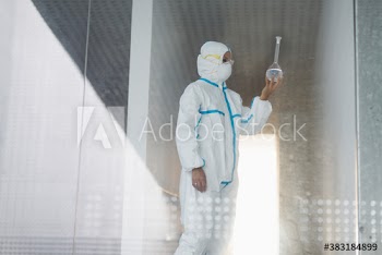 Biochemist in clean suit examining beaker with liquid in laboratory