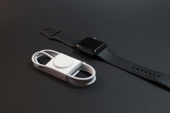 Black Aluminum Case Apple Watch With Sport Band Beside Magnetic Charger