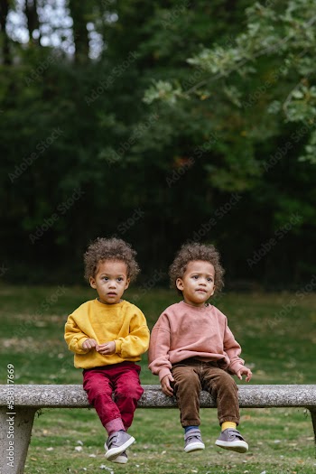 Black and Asian twins sitting together on bench in park 