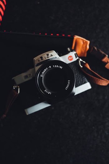 black and gray Leica bridge camera with brown sling on top of black textile