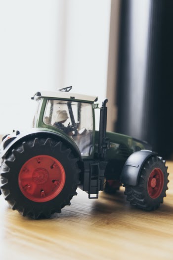 Black and Green Farm Tractor Toy on Brown Wooden Table Beside Window