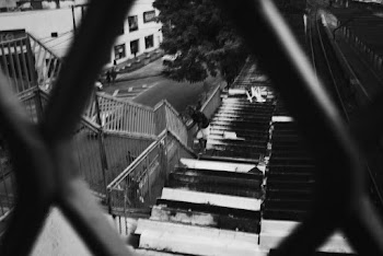 Black And White Photo Of A Man On The Roof Holding On High Steel Fence For Support