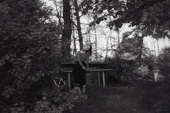 Black and White photo of a woman sitting on a bench in the middle of trees