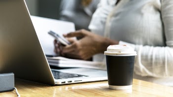 Black and White Plastic Coffee Cup Beside Gray Laptop Computer