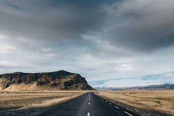 black asphalt road and brown mountain under gray and white sky during daytime