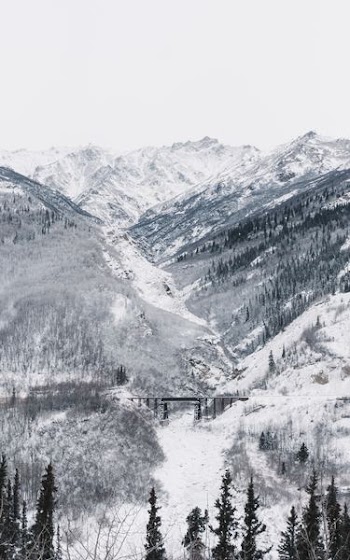 black bridge surrounded by mountain covered with snow under white sky