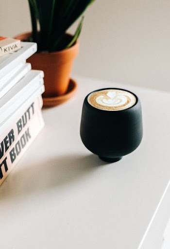 black ceramic teacup beside books and potted green plant on white wooden table