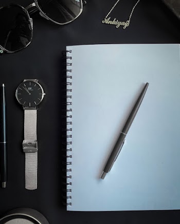 Black Click Pen Top Of A Spring Notebook Surrounded By Personal Effects
