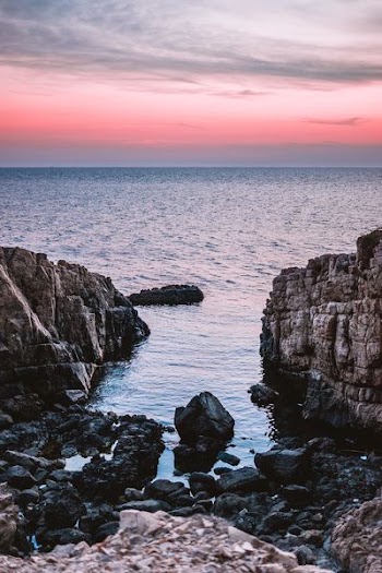 black concrete rocks beside sea under gray sky