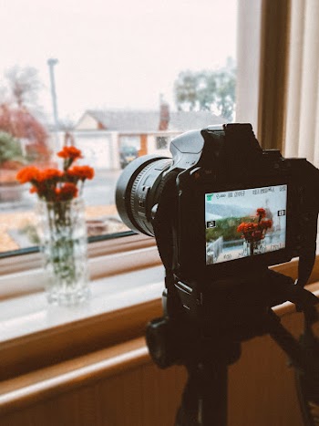 Black Dslr Camera Taking Photo of Orange Flowers in Clear Glass Flower Vase