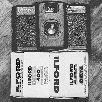 Black Lomo Compact Camera Beside Ilford Delta 400 Black &amp; White Film Box