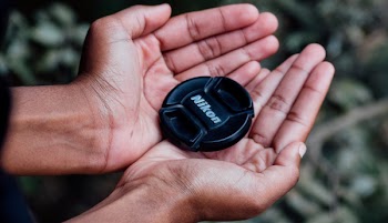 Black Nikon Camera Lens Cover on Left and Right Human Palms