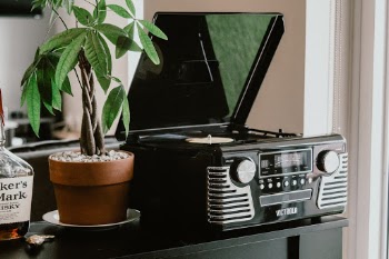 Black retro record player by Victrola next to green plant on black desk in living room.