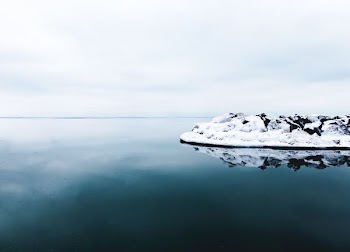 black rock formation covered with snow beside calm body of water