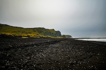 Black Sand Shore Near Green Grassy Hill