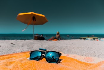 Black Sunglasses on Brown Blanket on Shore