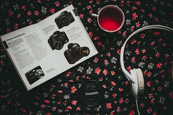 Black Tamron Zoom Lens Near White Headset, Mug, and Camera Manual