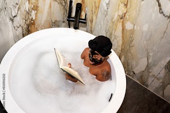 Black woman soaking in bathtub with mask on reading a book