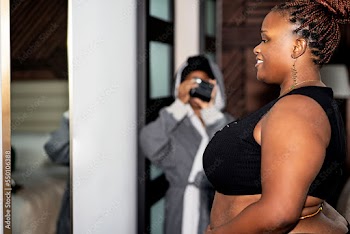 Black woman with braids wearing waistbeads admiring herself in the mirror