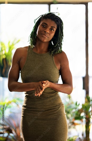 Black Woman with green dreadlocks in green dress surrounded by plants
