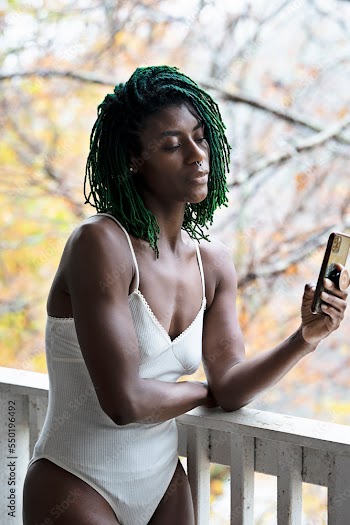 Black woman with green dreadlocks on the patio holding cell phone