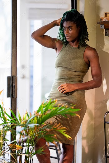 Black woman with green dreadlocks  wearing green dress standing in patio entrance