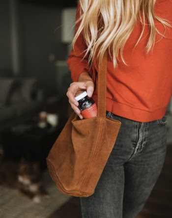 Blonde woman walking out of door as she puts a bottle of Nouri into her brown purse.