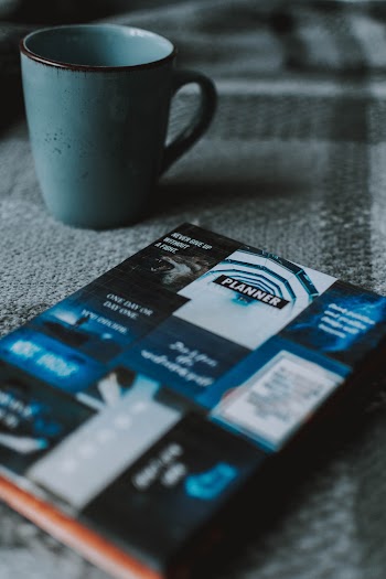 Blue and Black Planner Beside Ceramic Mug on Tabletop