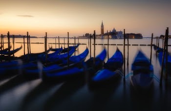 blue boats docking on calm body of water with castle in distance during sunrise