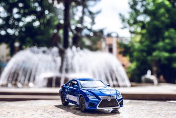 Blue Die-cast Toy Car Across Outdoor Fountain