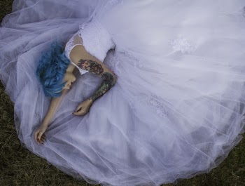 Blue Haired Woman in White Lace Wedding Dress Lying on Green Grasses