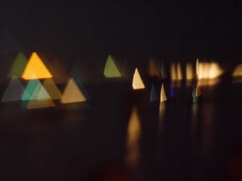 Boats floating on the water at night. Bokeh effect from a paper cutout, I love it because it's cute and calm and quaint.