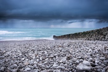 body of water across pebbles under dark sky