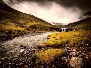 Body of Water and Green Grass Under Gray Sky