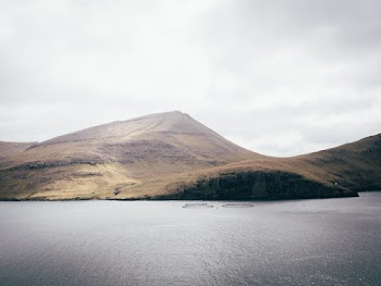 Body of Water and Mountain Under Grey Sky
