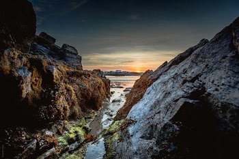 body of water between big rocks under gray and white sky at golden hour