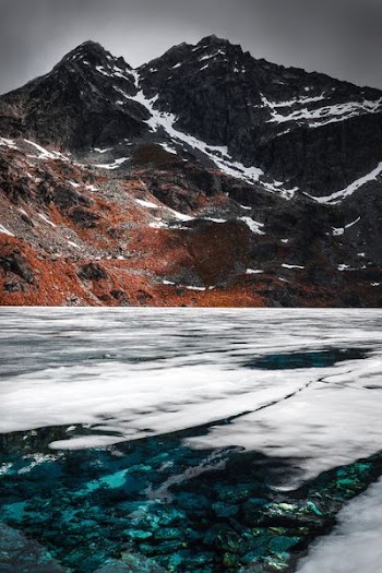 body of water near rocky mountain under gray sky