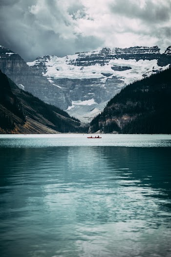 Body of Water Near Snow Covered Mountain Under Cloudy Sky