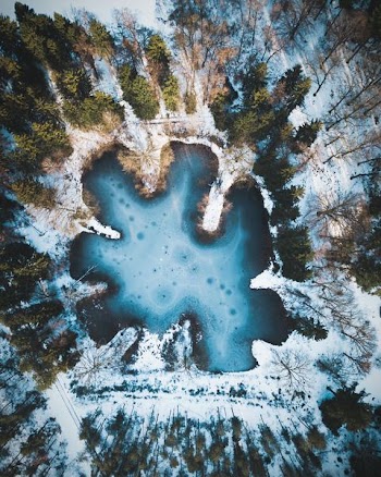 body of water surrounded by snow covered ground with green trees