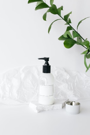 Bottle with cream on white table near houseplant