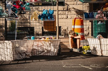 Boy Crouching and Resting Head on Hands and Knees Between Shelf of Plush Toys