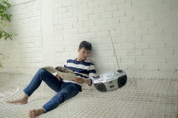 Boy Sitting Near Radio Holding White Catalog