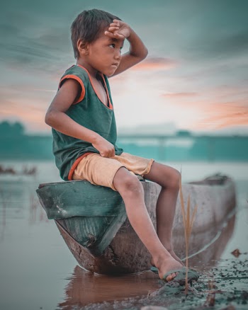 Boy Sitting on Canoe Near Body of Water Taken Under White Clouds